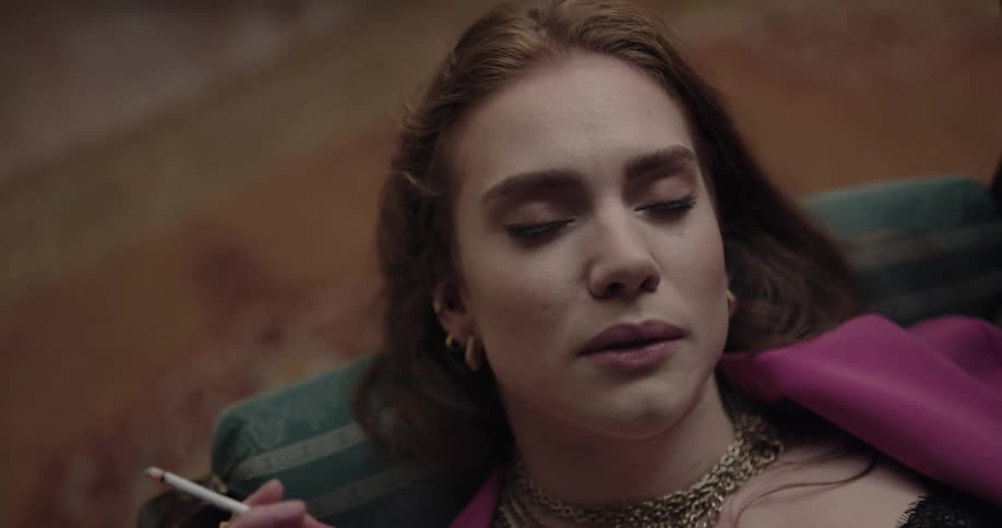 Woman leisurely smoking while resting reclined on a couch next to an elaborate rug