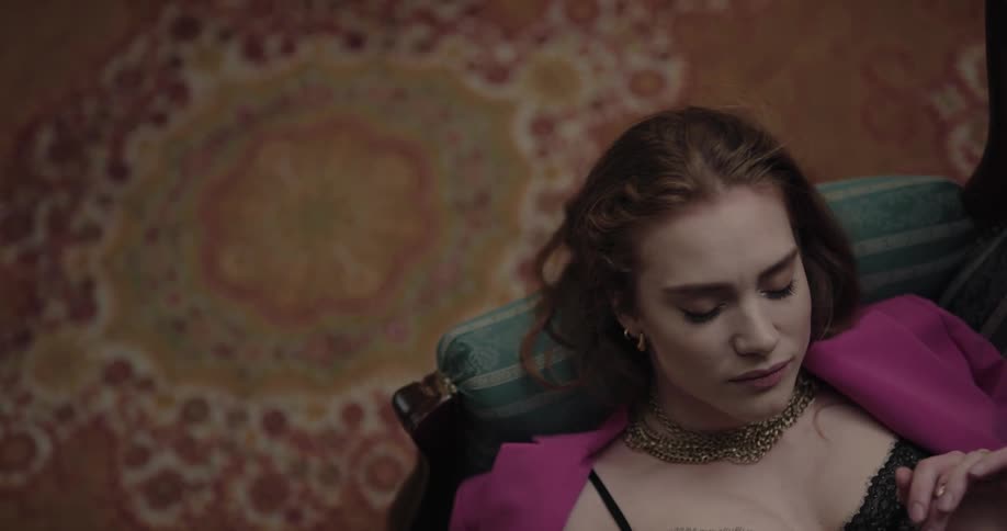 Woman leisurely resting reclined on a couch next to an elaborate rug