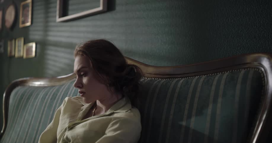 A frowning woman sits on a sofa lost in thought during the day