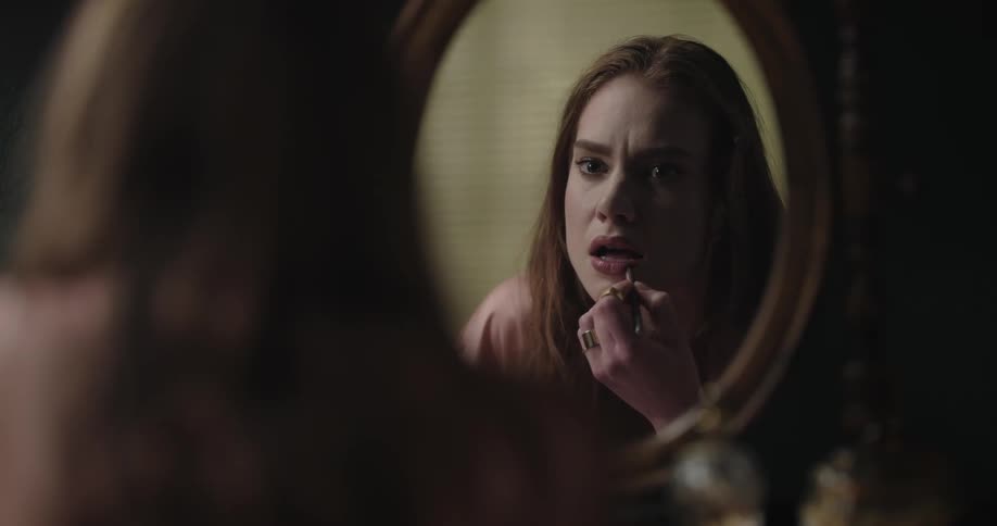 A woman puts on lipstick in the mirror