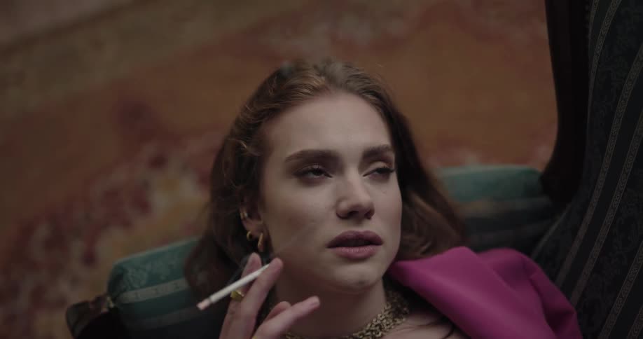 Contemplative young fancy beautiful woman lying on the couch smoking a cigarette