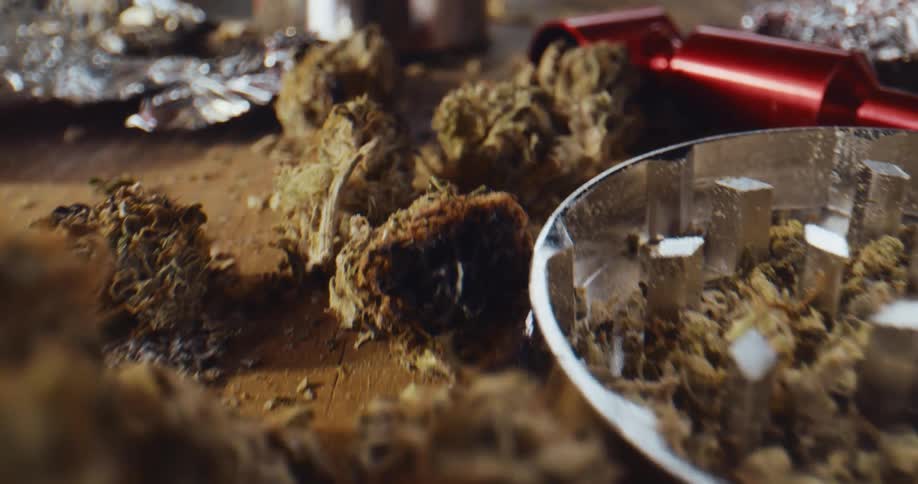 Marijuana buds lighter and grinder scattered across a wood table