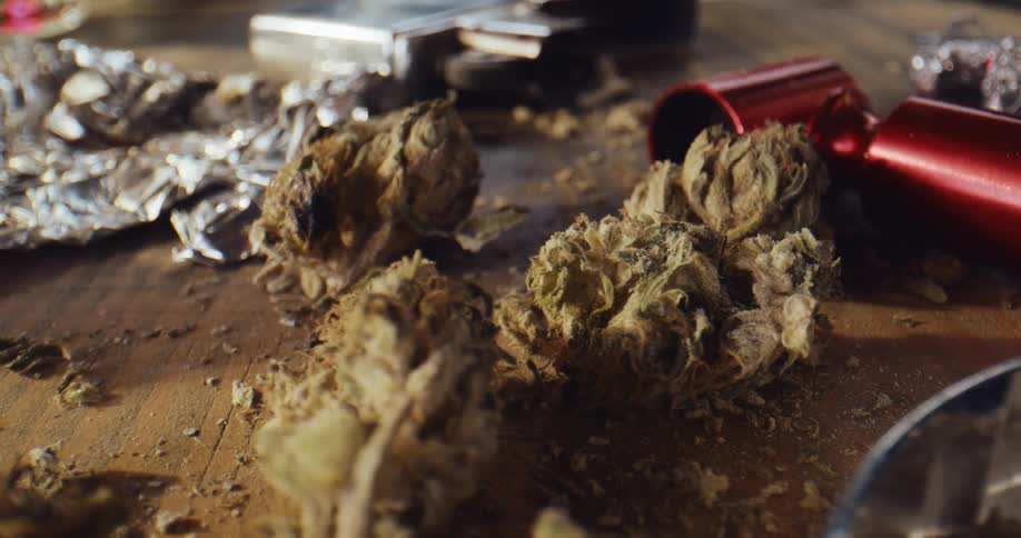 Close up of marijuana buds laying near on aluminum foil over a wooden table
