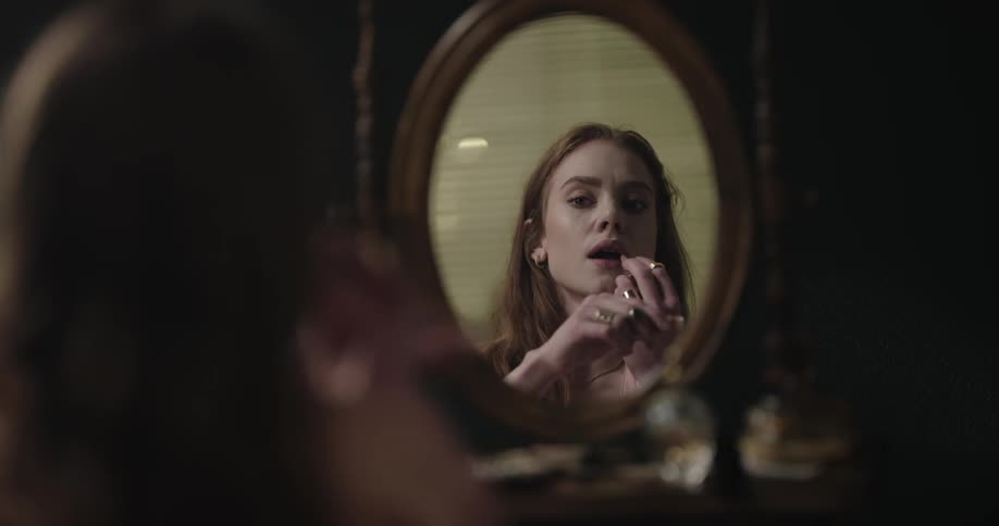 A woman applies lipstick in the mirror of a vanity