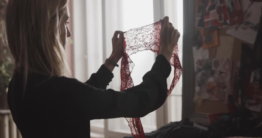 A woman examines a piece of frame while standing before a table indoors during the day