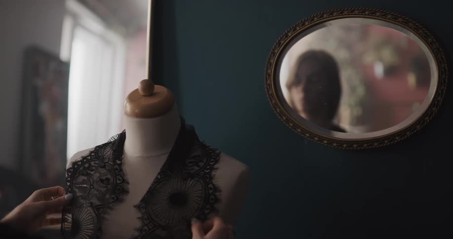 Mirror reflects woman as she places lace panel on dress form