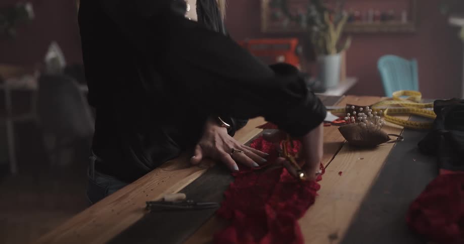 Female tailor cuts a piece of red fabric with scissors over a workbench