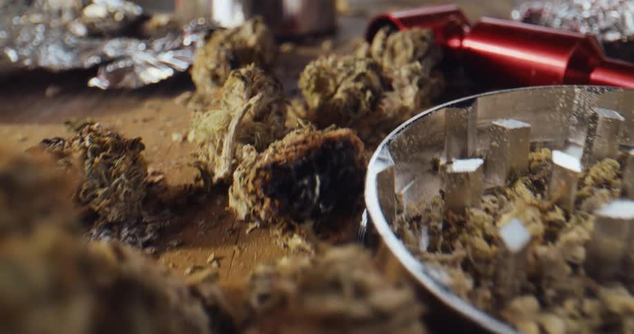 Close up of marijuana buds and drugs paraphernalia laying over a table