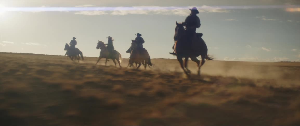 A group of people in cowboy hats ride horses quickly through a grassland during the day