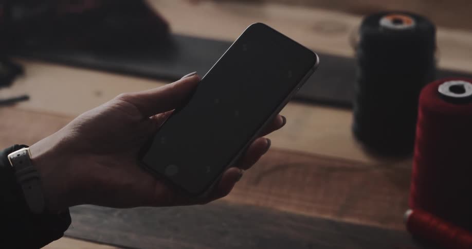 Person holds smartphone near large thread spools sitting on wooden slats of table