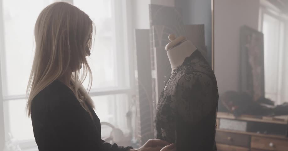 Female tailor fitting a dress on a mannequin inside her workshop