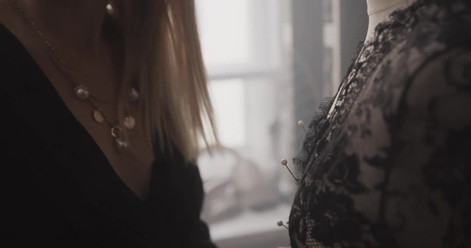A woman uses pins to fasten a garment to a mannequin indoors during the day