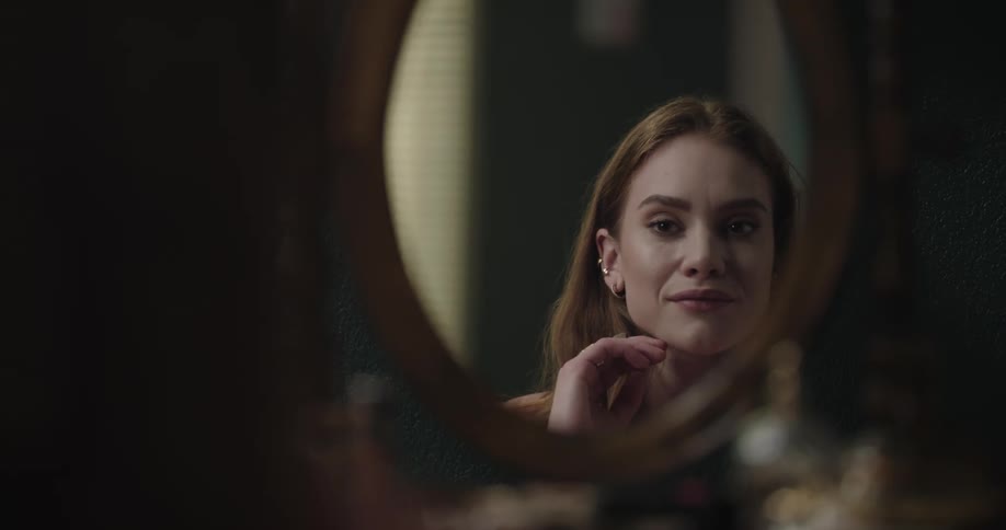 Young redhead woman checking herself in a round mirror on a dressing table
