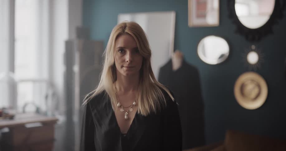 Blonde white woman standing in the middle of the room in front of a mannequin turning around and crossing her arms