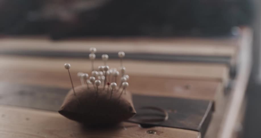 Tailor picks up pins from a pin cushion resting over a workbench