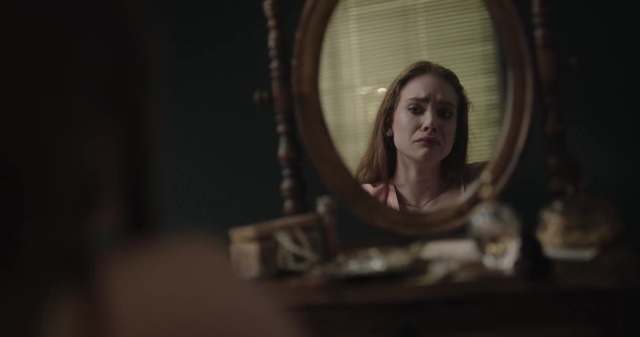Young woman crying while sitting in front of a dressing table removing her makeup in front of the mirror