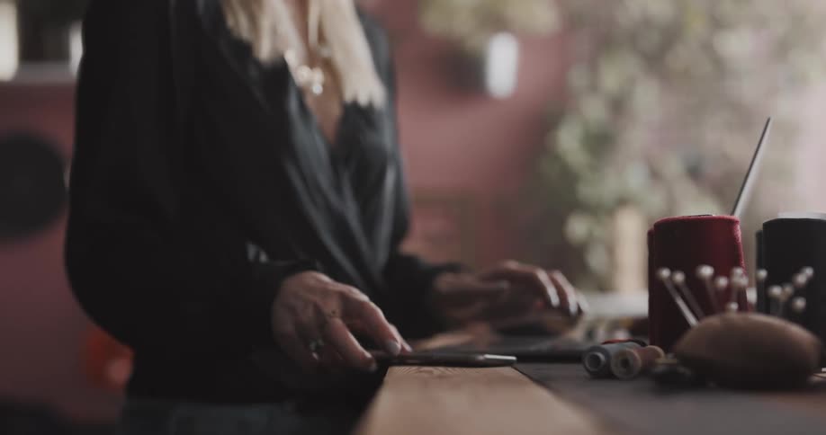 A woman is standing at a table typing on a laptop computer and she answers her cell phone and walks away