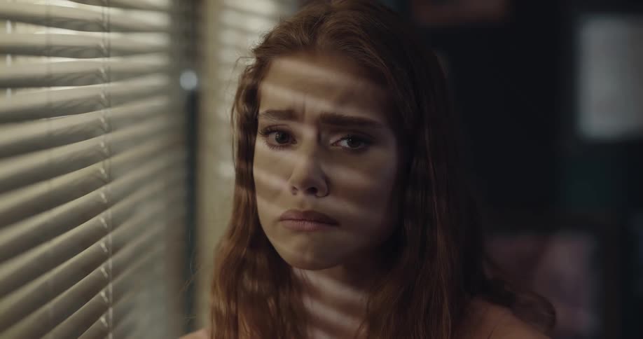 Sad young woman standing next to the window looking like she is about to cry