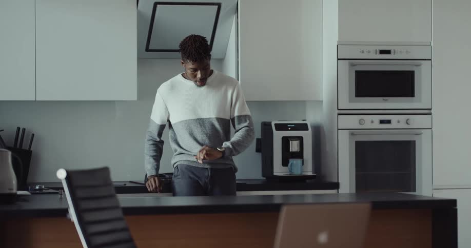 A man is walking in his kitchen and makes a cup of coffee