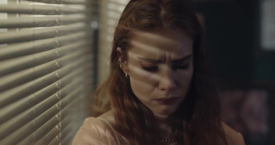 A woman looks upset and is standing near the window