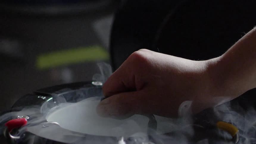 A hand is stirring something in a container with steam coming off it