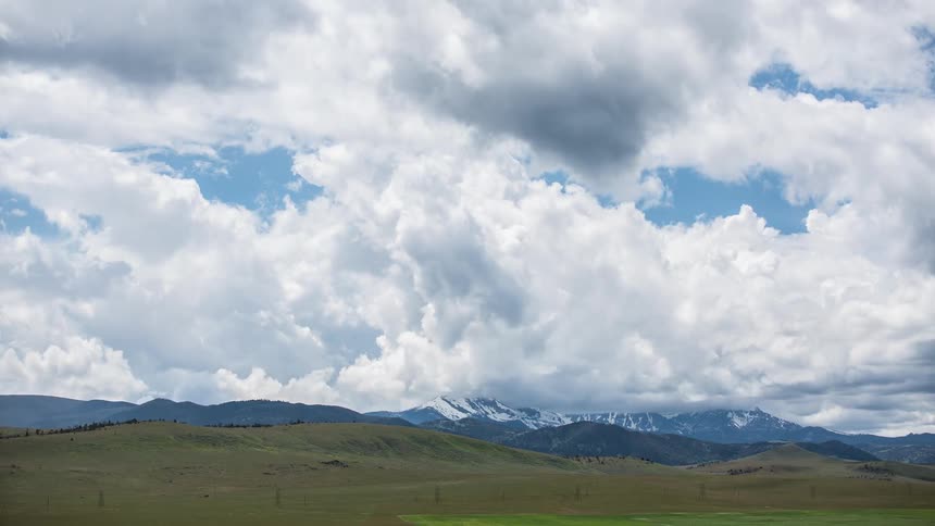 Cumulus clouds move across a blue sky and their shadows move across the ground below and there are mountains in the distance