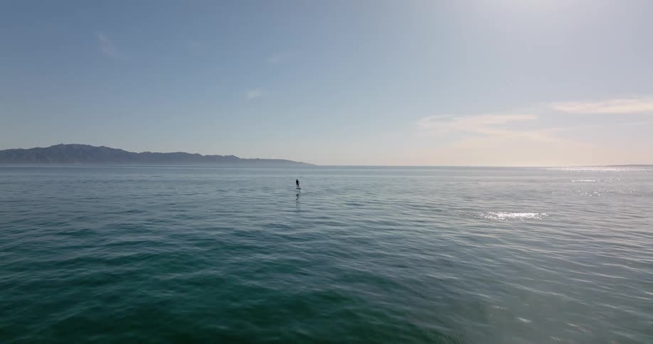 A person standing and skimming the shimmering water surface on a hoverboard