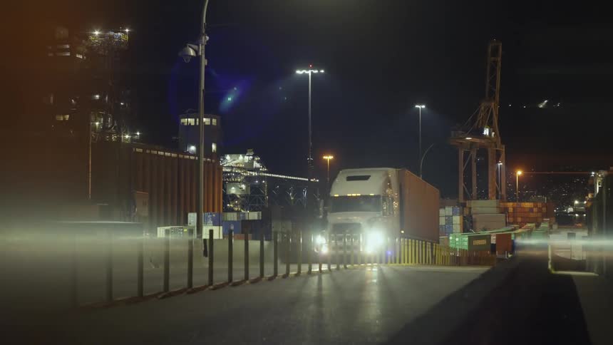 Shipping truck hauling a container out of a port at night