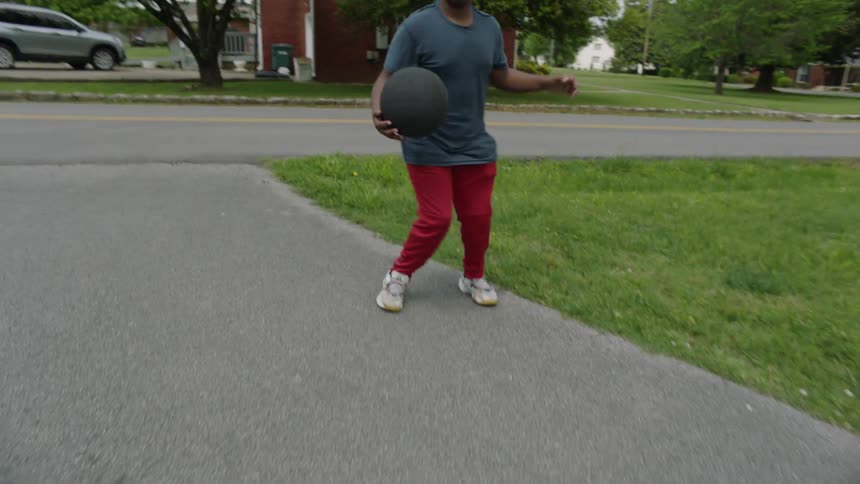 Teen boys playing basketball on the sidewalk in front of a house on a sunny day
