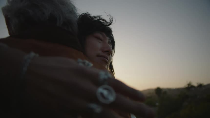 An adult son hugs his father tightly patting his shoulder with his hand
