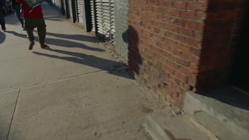 A man carrying his son down a city sidewalk casts a shadow on a brick wall