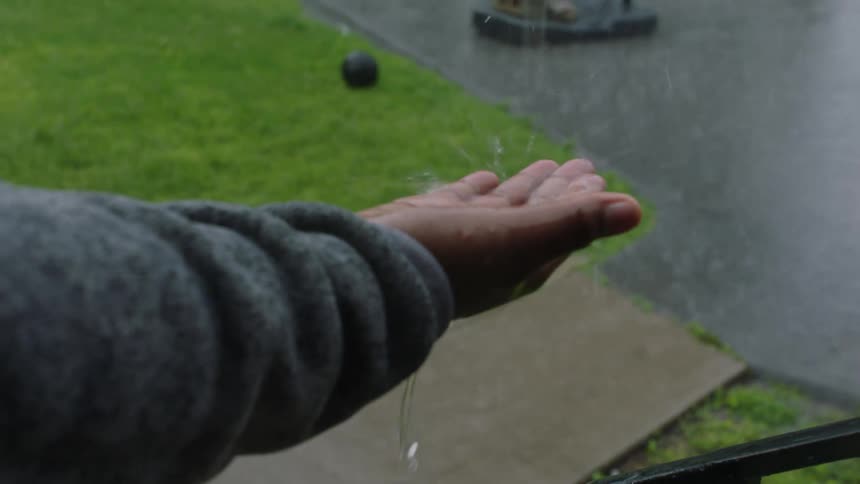 A child holds out his hand in the rain and raindrops splash in the palm of his hand