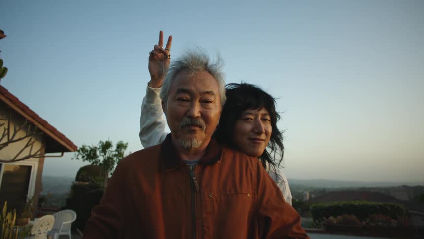 Asian elderly man and adult son posing for a photo while the son is giving bunny ears to the father behind his back