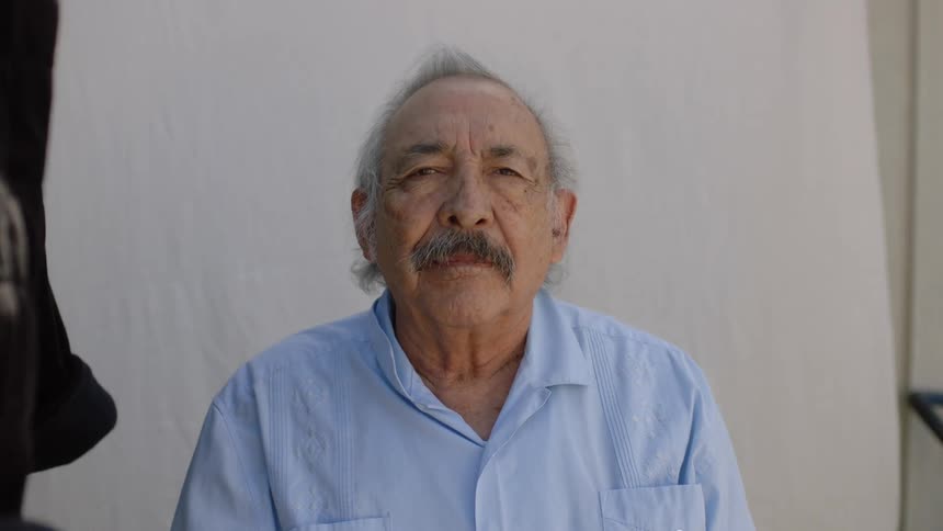 A man sitting for his picture to be taken with a white sheet hanging behind him