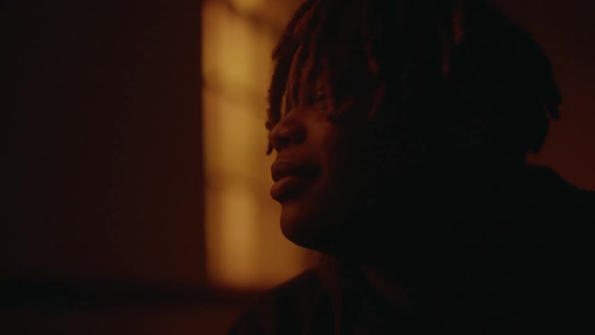 Face of a young man standing on a dimly lit room looking out a window