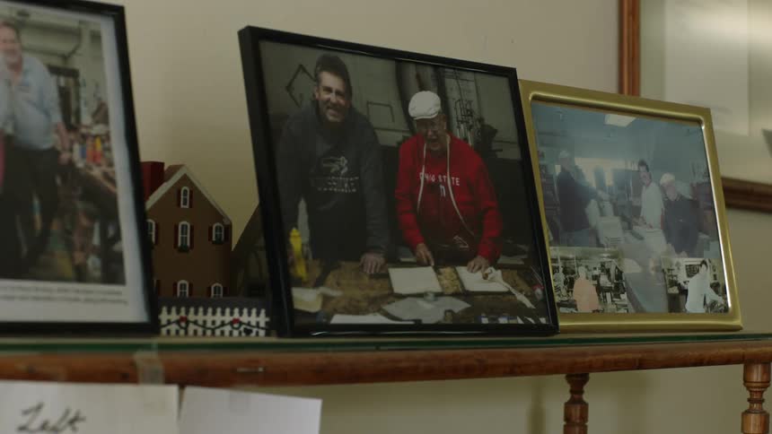 Framed photos of a family sit along a wooden shelf in a house