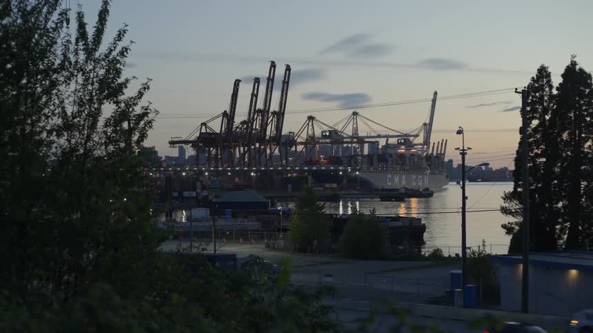 Vehicles drive along a coastal road across from a shipping yard