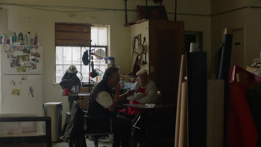 Father and son sit at a table in the back room smoking