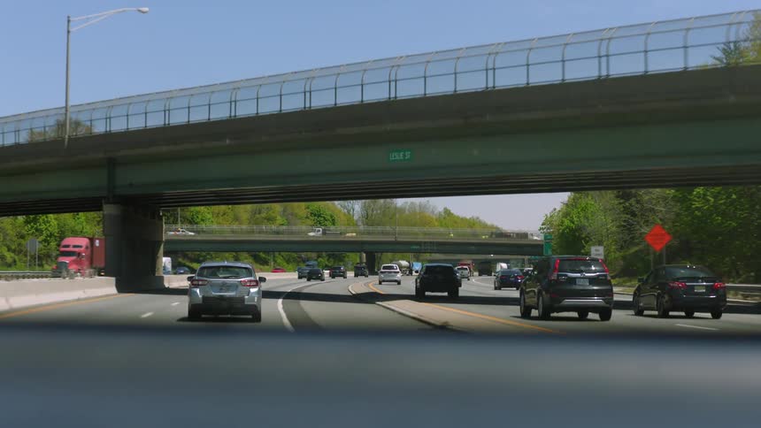 Traffic moves on a highway through an underpass and towards another underpass on a clear day