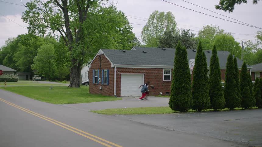 Two boys play basketball in their driveway as a car passes through the neighborhood