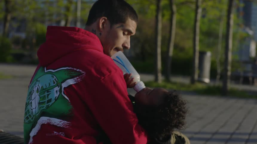 Father feeding his son with a bottle on a park in the morning