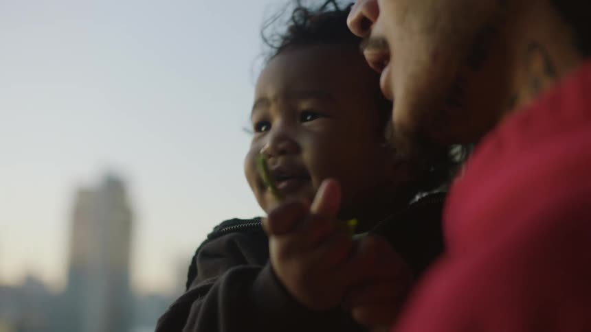 Father holding his son on his arms in front of the city skyline at morning