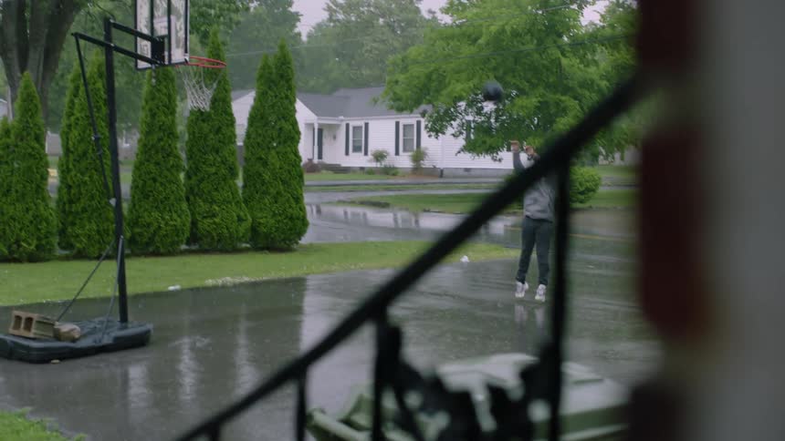 Youth plays basketball in driveway while it rains