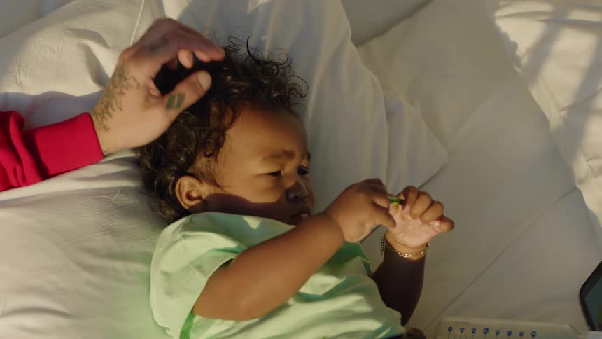 Father with tattooed hand strokes head of child lying in bed