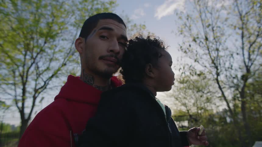 Father carries child who is holding food with pedestrians and water in the background