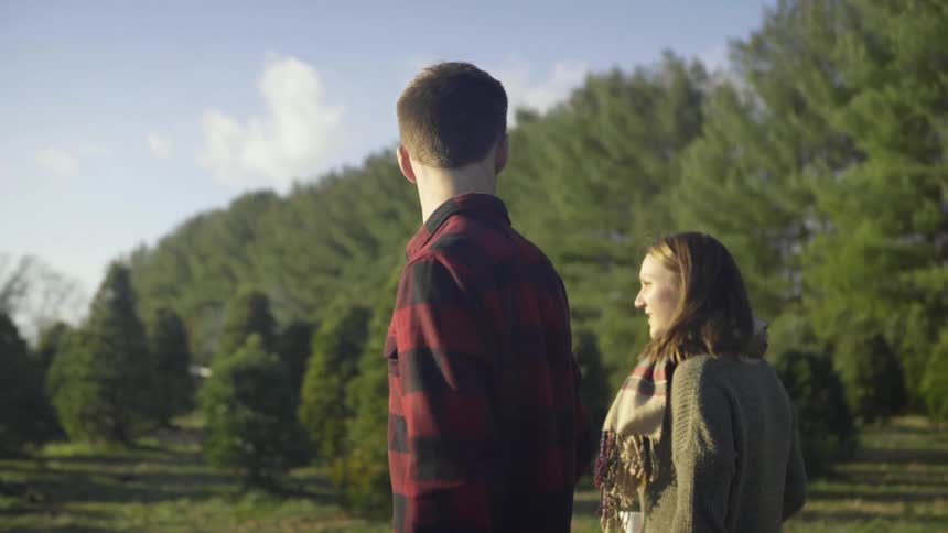 A man holding a saw points out a tree to a woman
