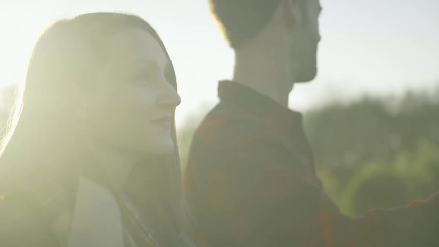 A couple are smiling and walking through a field of christmas trees