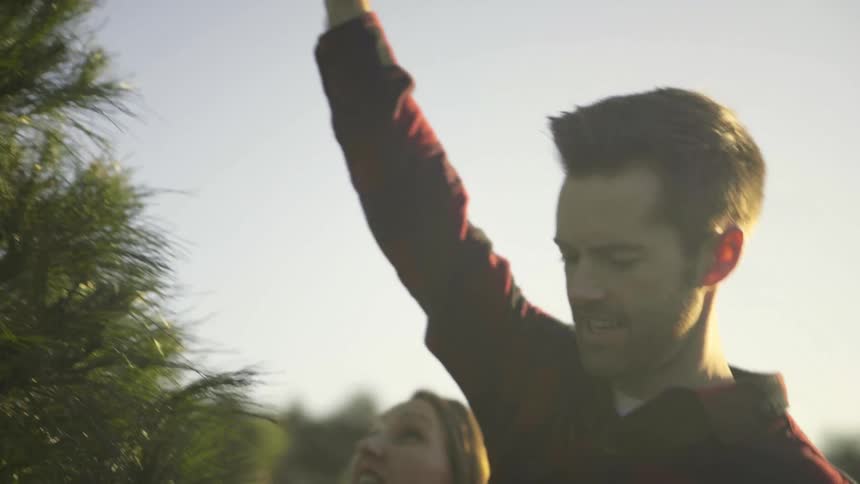 A man and woman hold their hands up to measure a christmas tree before cutting it down