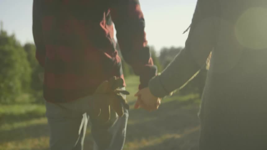 Man and woman hold hands and walk in a tree lot