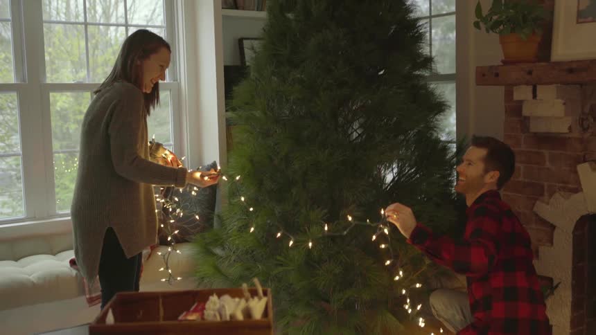 A man and woman decorate a christmas tree